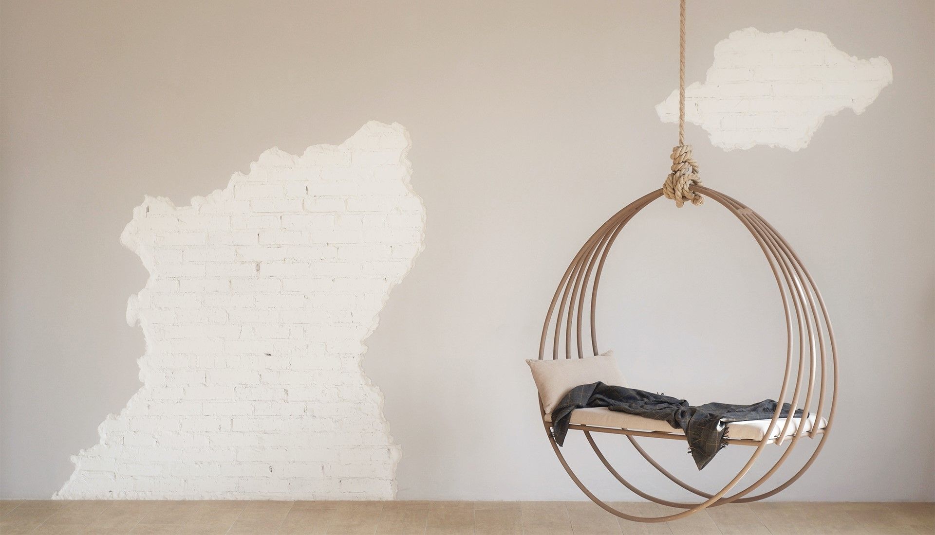 Hängesessel aus Holz in runder Form, mit einem Kissen und einer Decke, vor einer Wand mit unregelmäßigen weißen Putzstellen.